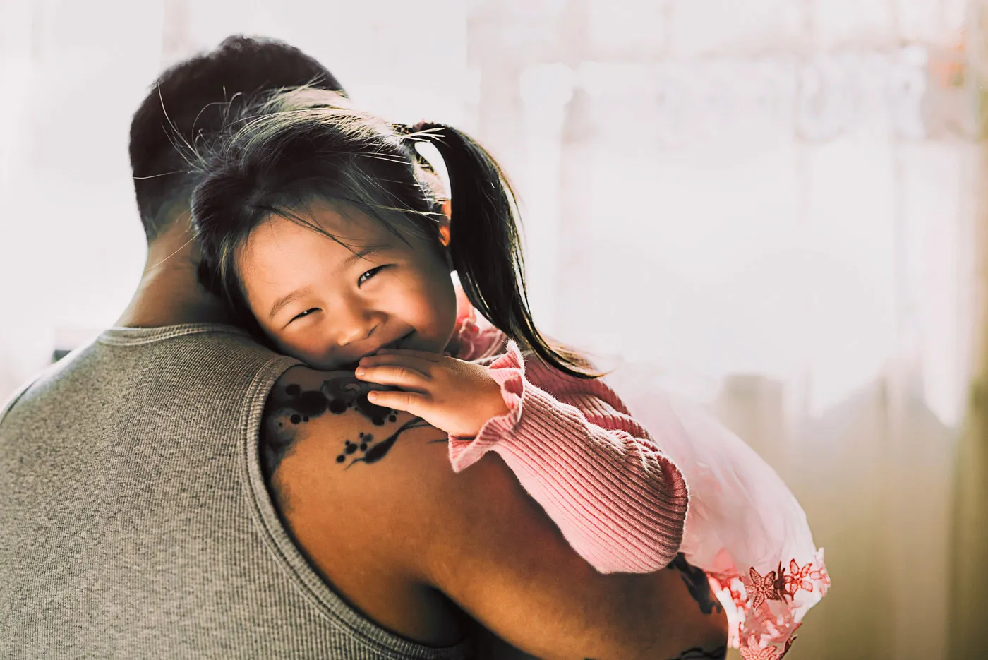 Child leans on parents shoulder and smiles at camera