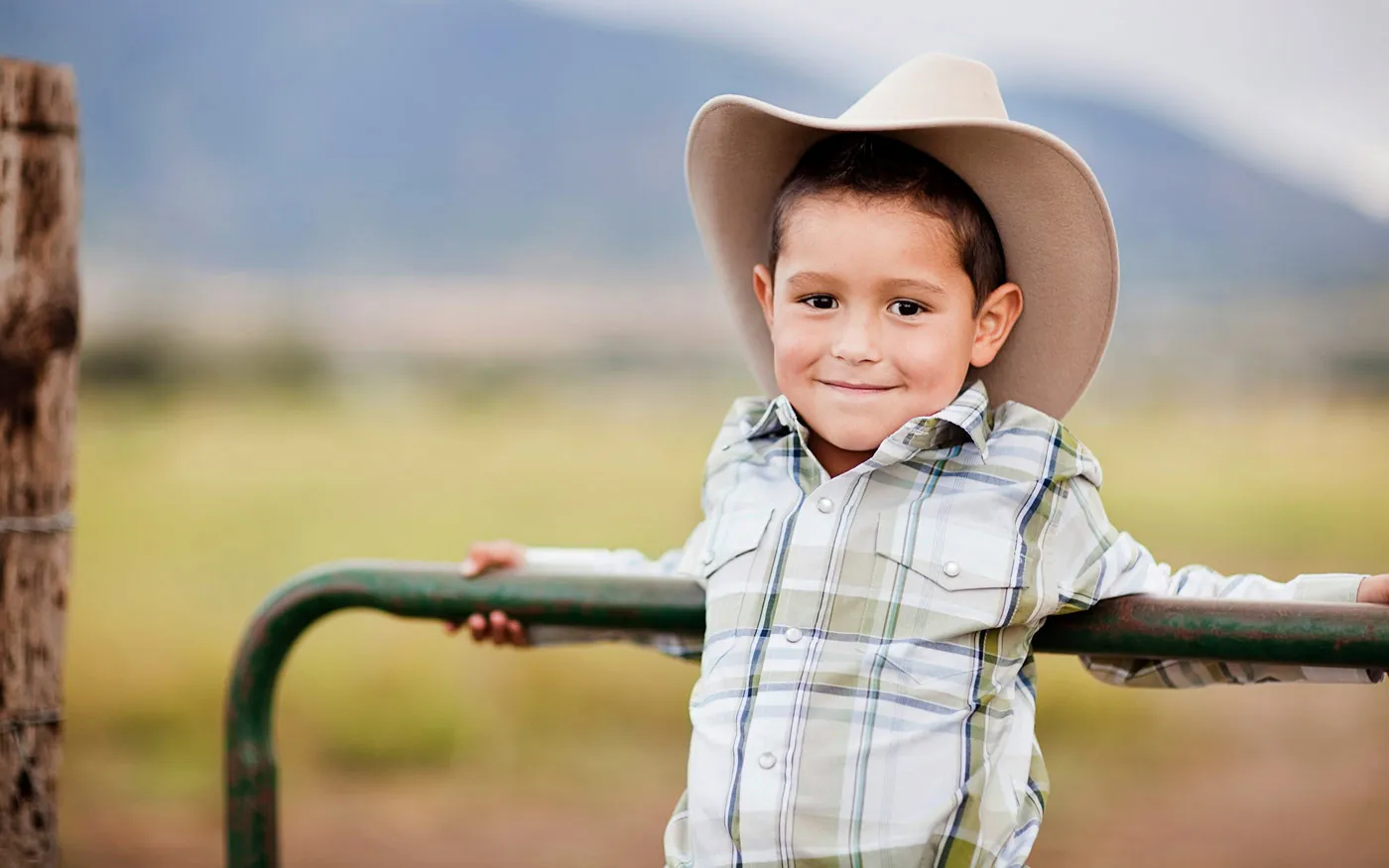 Young boy in a cowboy hat leaning against a fence.
